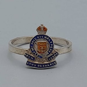 May include: A silver ring with a blue and orange enamel Royal Army Ordnance Corps crest. The crest features a crown, a shield with a lion, and the words "Royal Army Ordnance Corps".