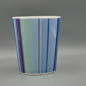 Può includere: Un porta spazzolino da denti in ceramica bianca con un motivo a strisce blu, verdi e viola.