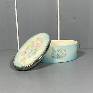 May include: A blue and white oval trinket box with a floral design. The lid is open and the box is sitting on a gray surface.