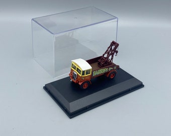 May include: A red and yellow toy truck with a white cab and a crane on the back. The truck is labeled "HARRIS'S GARAGE". The truck is displayed on a black base inside a clear plastic display case.
