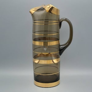 May include: A brown glass jug with gold stripes. The jug has a wide mouth and a handle.
