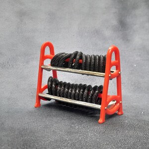 K&ouml;nnte beinhalten: Ein kleiner, roter St&auml;nder mit zahlreichen kleinen schwarzen Reifen. Der St&auml;nder hat zwei Ebenen mit silbernen Metallstangen und besteht aus leuchtend rotem Kunststoff. Die Reifen sind ordentlich angeordnet.