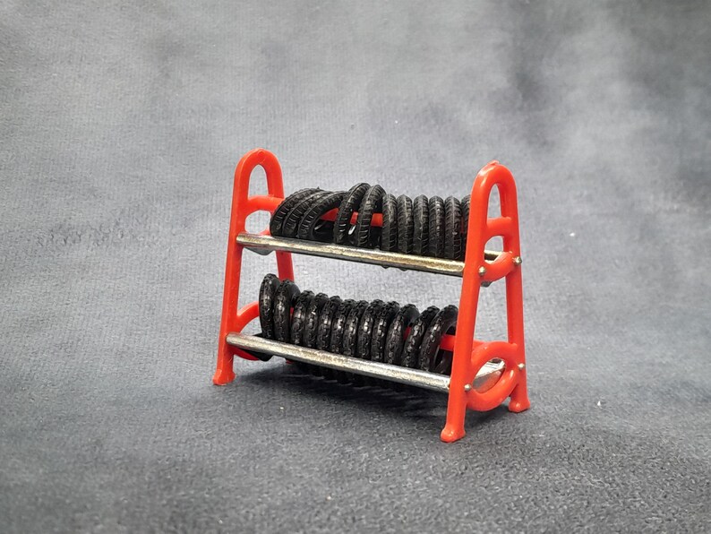 K&ouml;nnte beinhalten: Ein kleiner, roter St&auml;nder mit zahlreichen kleinen schwarzen Reifen. Der St&auml;nder hat zwei Ebenen mit silbernen Metallstangen und besteht aus leuchtend rotem Kunststoff. Die Reifen sind ordentlich angeordnet.