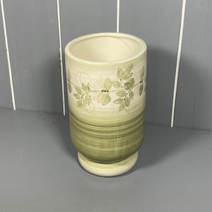 May include: A ceramic vase with a green and white floral design. The vase has a wide mouth and a rounded base.