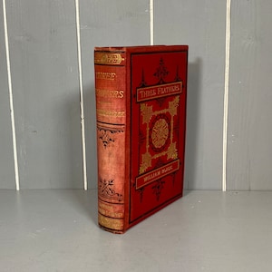 May include: A red hardback book titled "Three Feathers" by William Black. The book has gold lettering and decorative designs on the cover.