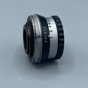 Pu&ograve; includere: Un obiettivo per macchina fotografica nero e argento con i numeri 331073 e 2 4 816 32 stampati sul lato.