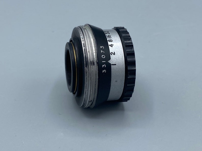 Pu&ograve; includere: Un obiettivo per macchina fotografica nero e argento con i numeri 331073 e 2 4 816 32 stampati sul lato.