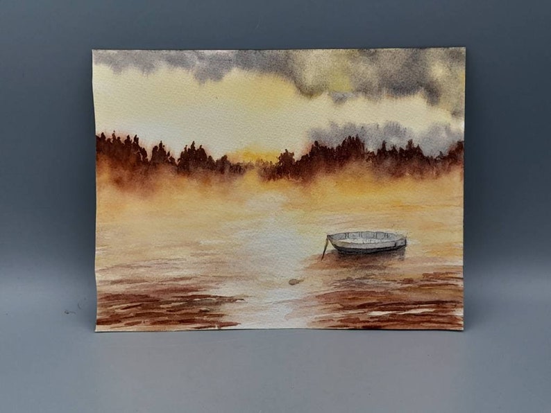 May include: A watercolor painting of a small boat on a lake with a foggy, golden sunset in the background.