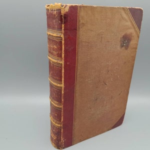 May include: A vintage, brown leather-bound book with red and gold accents. The book is closed and has a worn, aged appearance.