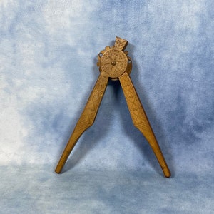 May include: A wooden nutcracker with intricate carvings. The nutcracker is shaped like a pair of pliers with a circular, carved centre.