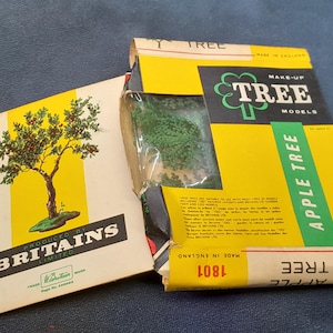 Peut inclure: Kit de modèle "Apple Tree" vintage de Britains Limited. La boîte jaune et verte porte les mots "MAKE-UP TREE MODELS" et "APPLE TREE". Le kit comprend un livret avec une illustration d'arbre et le texte "PRODUCED BY BRITAINS LIMITED".
