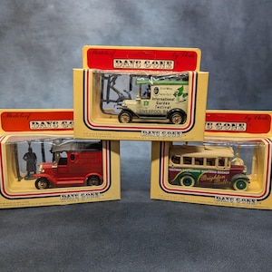 May include: Three boxed Days Gone model vehicles. The models are a red truck, a cream-colored truck with "International Garden Festival Liverpool 84" text, and a bus with "Brighton Belle" text.