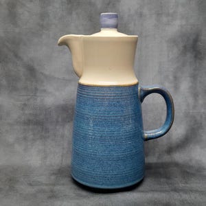 Könnte beinhalten: Eine blaue und weiße Kaffeekanne aus Keramik mit Deckel und Henkel. Die Kanne hat eine strukturierte blaue Oberfläche und ein weißes Oberteil.