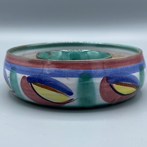 May include: A ceramic serving bowl with a green, blue, red, and yellow geometric design. The bowl has a raised center section.