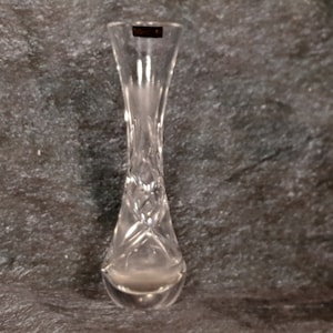 May include: A clear glass bud vase with a cut glass design. The vase is approximately 6 inches tall.