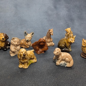 Puede incluir: Una colección de diez pequeñas figuras de animales de cerámica que incluye un perro, un oso, un ciervo, una jirafa, un orangután, un zorro, un búho y otras criaturas. Cada pieza presenta un acabado brillante en tonos naturales marrón, beige y crema.