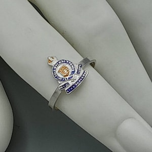 May include: A silver ring with a blue and gold enamel design. The design features a crown, a lion, and the words "Royal Military Police".