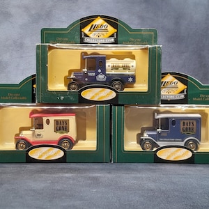 May include: Die-cast model collectible trucks in their original boxes. The trucks are in blue, white, and red, with the words "DAYS GONE" printed on the sides. The boxes are green with the "LEDO COLLECTORS CLUB" logo.
