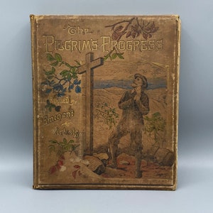 May include: The cover of an antique book titled "The Pilgrim's Progress" illustrated by eminent artists. The cover features a man standing in a landscape with a cross in the background.