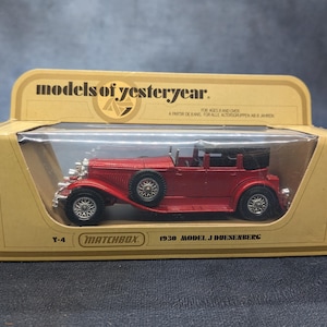 May include: A red 1930 Model J Duesenberg toy car in its original packaging. The Matchbox Y-4 model is in a cardboard box with the words "models of yesteryear" printed on the top. The car has a black roof and silver wheels.