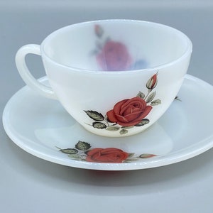 May include: A white porcelain teacup and saucer set with a floral design featuring red roses and green leaves.