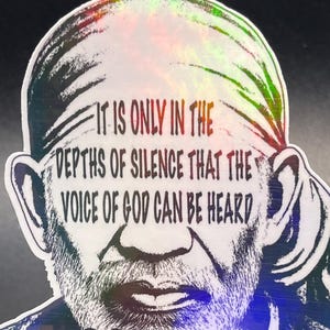 May include: A holographic sticker featuring an illustration of Sai Baba with the text "IT IS ONLY IN THE DEPTHS OF SILENCE THAT THE VOICE OF GOD CAN BE HEARD". The sticker is displayed on a clear plastic stand.
