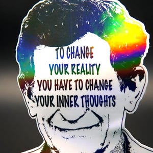 May include: A sticker featuring a portrait of David Bohm with a rainbow-colored hair design. The sticker includes the quote "TO CHANGE YOUR REALITY YOU HAVE TO CHANGE YOUR INNER THOUGHTS" and the name "DAVID BOHM".
