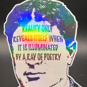 May include: Holographic sticker featuring a portrait of Georges Braque with the quote "REALITY ONLY REVEALS ITSELF WHEN IT IS ILLUMINATED BY A RAY OF POETRY." The sticker has a clear stand and a black background.