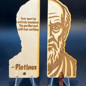 May include: Two wooden bookends with a quote by Plotinus. One bookend features the quote "Fear must be entirely banished. The purified soul will fear nothing." The other bookend has a portrait of Plotinus. Each bookend is supported by a clear plastic stand.