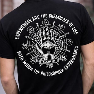 May include: Black t-shirt featuring a white graphic of a man's portrait with the word "ALCHEMY" below it. The back of the shirt has a circular design with text that reads "EXPERIENCES ARE THE CHEMICALS OF LIFE".
