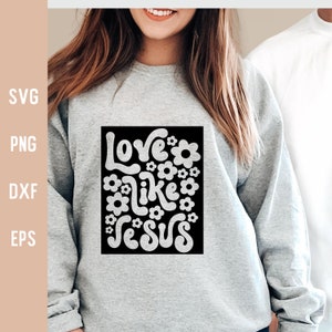 K&ouml;nnte beinhalten: Ein graues Sweatshirt mit einer schwarzen quadratischen Grafik, auf der in Wei&szlig; "Love like Jesus" steht, umgeben von wei&szlig;en Blumen.