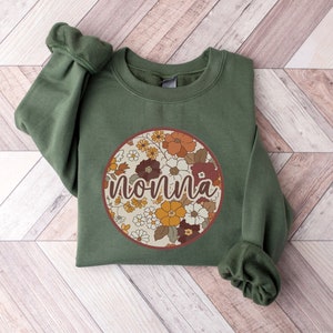 May include: A green sweatshirt with a round floral print and the word "nonna" in a brown font.