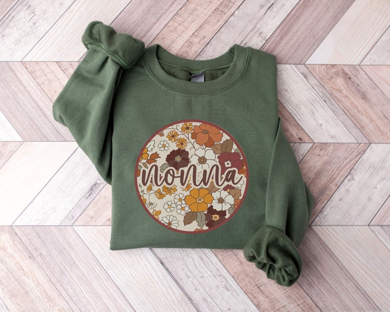 May include: A green sweatshirt with a round floral print and the word "nonna" in a brown font.