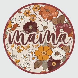 May include: A round, cream-colored background with a floral pattern in shades of orange, brown, and white. The word "mama" is written in a brown cursive font in the center of the circle.