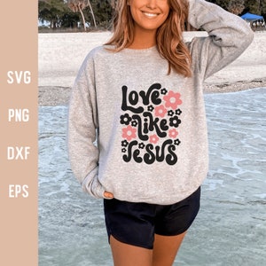 K&ouml;nnte beinhalten: Ein graues Sweatshirt mit dem Text "Love like Jesus" in Schwarz und Rosa mit floralen Akzenten.