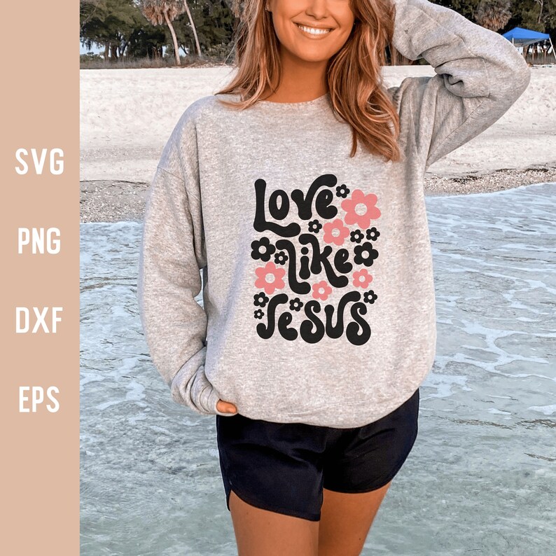 K&ouml;nnte beinhalten: Ein graues Sweatshirt mit dem Text "Love like Jesus" in Schwarz und Rosa mit floralen Akzenten.