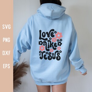 K&ouml;nnte beinhalten: Ein hellblauer Hoodie mit einer schwarzen Grafik, auf der "Love like Jesus" mit rosa Blumen um den Text steht.