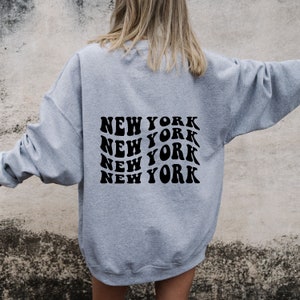 May include: Grey sweatshirt with a black graphic print of the words "NEW YORK" repeated four times in a retro style.