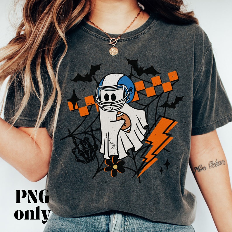 Puede incluir: Una camiseta gris con un fantasma que lleva un casco de f&uacute;tbol americano y sostiene un bal&oacute;n de f&uacute;tbol. El fantasma est&aacute; rodeado de murci&eacute;lagos, rayos y una telara&ntilde;a. El texto "More Ocean" es visible en la manga derecha.