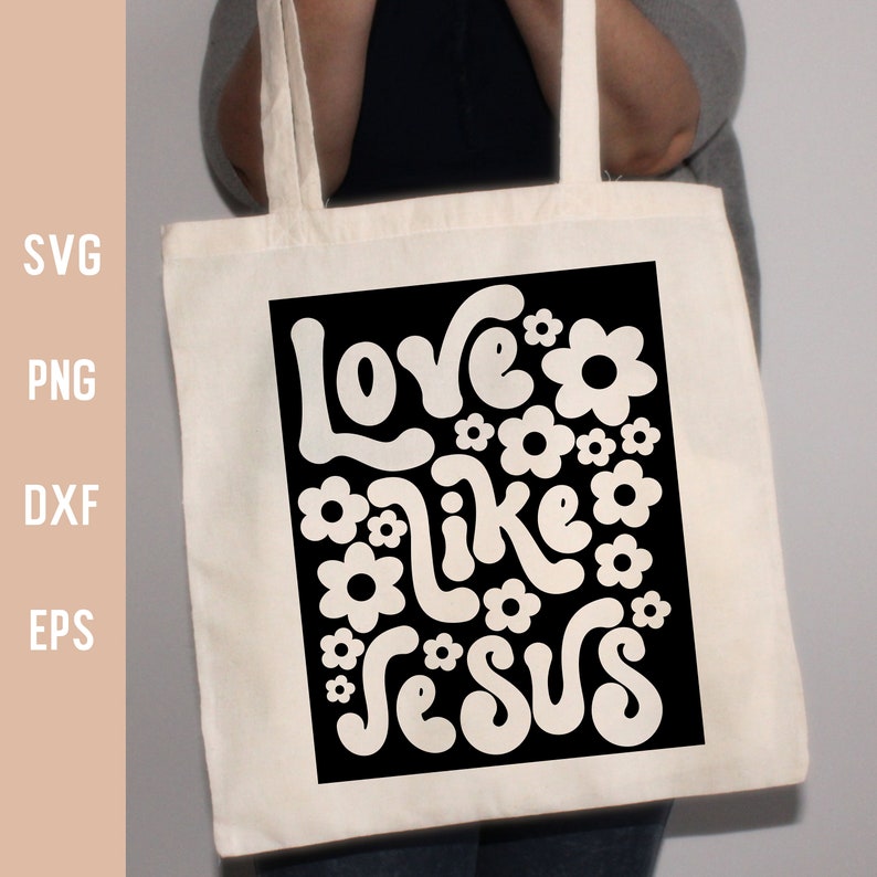 K&ouml;nnte beinhalten: Eine wei&szlig;e Einkaufstasche mit schwarzen Henkeln und einem schwarzen Design auf der Vorderseite. Das Design zeigt den Text "Love like Jesus" in einer Retro-Groovy-Schriftart mit wei&szlig;en Blumen, die den Text umgeben.