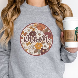 May include: Gray sweatshirt with a floral circle design and the word "mom" in a retro font.