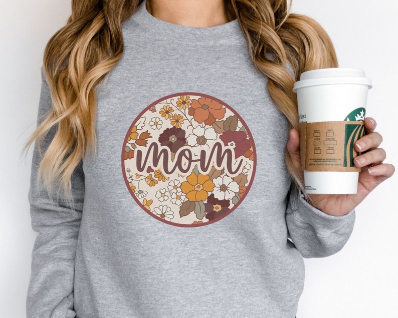 May include: Gray sweatshirt with a floral circle design and the word "mom" in a retro font.