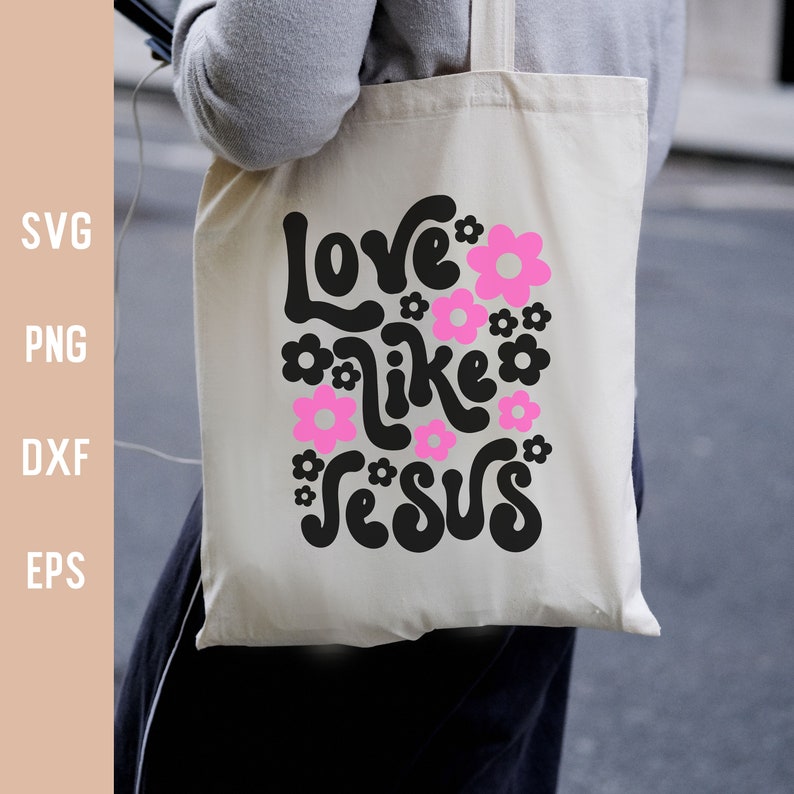 K&ouml;nnte beinhalten: Eine wei&szlig;e Einkaufstasche mit schwarzem Text, der "Love like Jesus" lautet, umgeben von rosa Blumen.