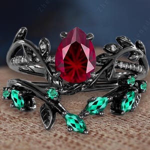 Vintage päron fyrverkerislipad rubin förlovningsring i svart guld med trådlindad friarring i kluster av smaragdblad, kvistförstärkt stapelformad vigselring