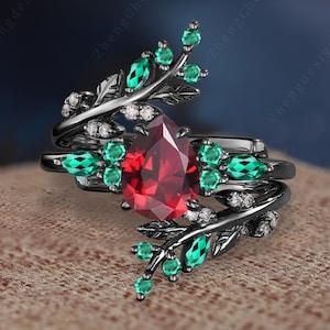 Op de afbeelding: Zwarte ring met een grote rode edelsteen omringd door kleinere groene edelstenen en een bladontwerp.