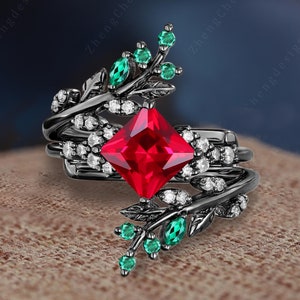 Pode incluir: Anel preto com uma grande pedra preciosa quadrada vermelha e pedras preciosas brancas menores. O anel tem uma banda de metal preto com um design de folhas e acentos verdes.
