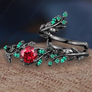 Può includere: Anello nero con una pietra rossa e foglie verdi. L'anello è progettato per avvolgersi attorno al dito.