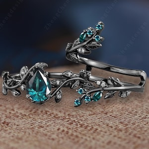 Puede incluir: Dos anillos negros con diseños de hojas y vides. Un anillo presenta una piedra preciosa de color verde azulado en forma de pera, mientras que el otro tiene piedras verde azulado más pequeñas. Ambos anillos tienen pequeñas piedras de acento transparentes.
