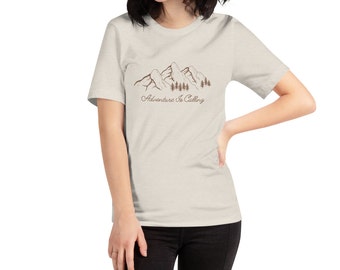 May include: A light beige t-shirt featuring a brown mountain range and trees graphic with the text "Adventure is Calling".
