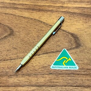 May include: A gold mechanical pencil with a silver clip and a black tip. The pencil is lying on a wooden surface. A green triangle sticker with a kangaroo and the text "AUSTRALIAN MADE" is in the background.